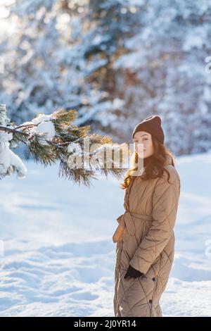 Bonne jeune femme marche dans la forêt parmi les pins couverts de neige en hiver ensoleillé. Banque D'Images