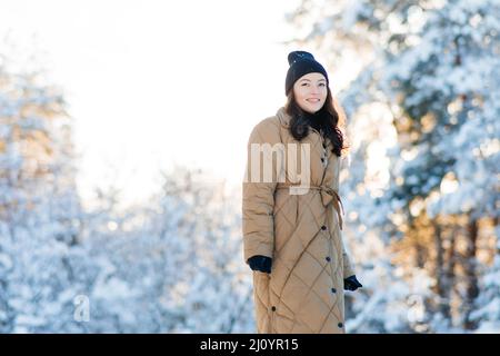 Bonne jeune femme souriante marche dans la forêt parmi les pins couverts de neige en hiver ensoleillé. Banque D'Images