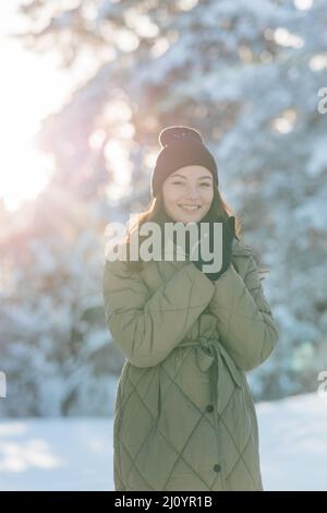 Bonne jeune femme souriante marche dans la forêt parmi les pins couverts de neige en hiver ensoleillé. Banque D'Images