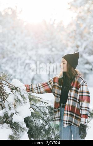 Bonne jeune femme marche dans la forêt parmi les pins couverts de neige en hiver ensoleillé. Banque D'Images