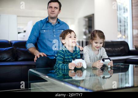 Jeune homme souriant jouant au jeu vidéo avec son fils et sa fille dans un salon moderne regardant à l'écran pendant le jeu. Passer du temps en famille ensemble Banque D'Images