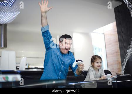 Jeune homme souriant jouant au jeu vidéo avec petite fille dans le salon moderne regardant à l'écran pendant le jeu. Passer du temps en famille ensemble Banque D'Images