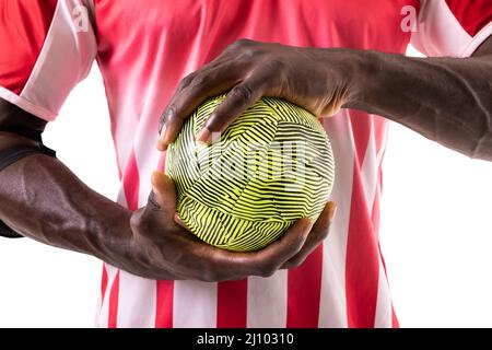 Section médiane d'un homme afro-américain de handball portant l'uniforme rouge tenant le ballon vert Banque D'Images