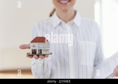 Vue de face smiley défocused femme Realtor montrant la maison miniature Banque D'Images