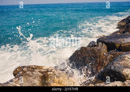 L'eau de mer bat contre les rochers rocheux et fait des vagues avec mousse Banque D'Images