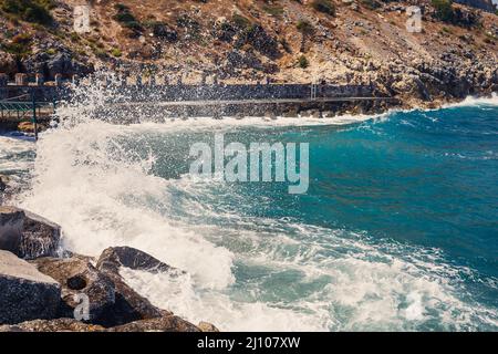 L'eau de mer bat contre les rochers rocheux et fait des vagues avec de la mousse, quai robuste dans la mer Banque D'Images