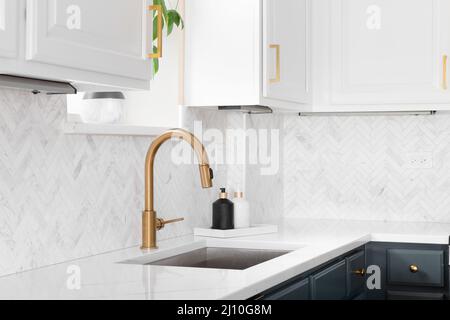 Détail lavabo dans une cuisine de luxe avec carreaux de dosseret à chevrons. Comptoir en marbre blanc et robinet en or. Banque D'Images