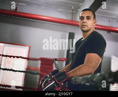 Ne vous gâchez pas. Portrait d'un jeune boxeur homme confiant appuyé contre des cordes à l'intérieur d'un anneau de boxe dans une salle de gym pendant la journée. Banque D'Images