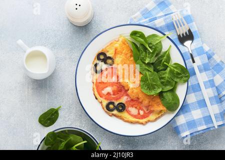 Omelette aux tomates, olives noires, fromage cottage et herbes aux épinards verts sur plaque blanche sur fond de béton gris. Délicieux petit déjeuner. En bonne santé Banque D'Images