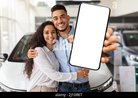 Famille musulmane aimant montrant un smartphone avec écran vierge, achetant la voiture Banque D'Images