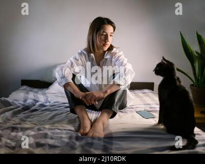 Femme assise sur le lit le soir avec un chat Banque D'Images