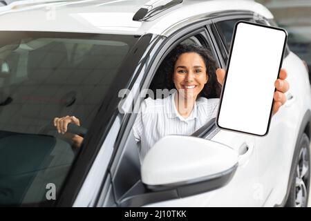 Femme positive du Moyen-Orient assise en voiture, montrant un smartphone Banque D'Images