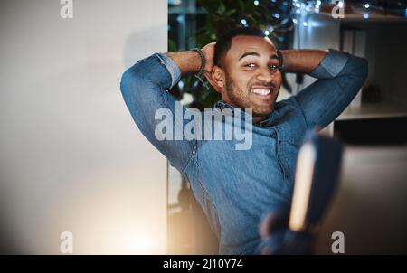 Je suis resté tard pour ce moment précis. Portrait d'un jeune homme d'affaires prenant une pause à son bureau dans un bureau moderne. Banque D'Images