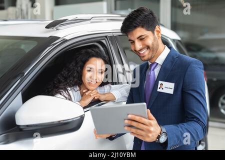 Jolie dame assise à l'intérieur de la voiture, ayant une conversation avec un vendeur Banque D'Images