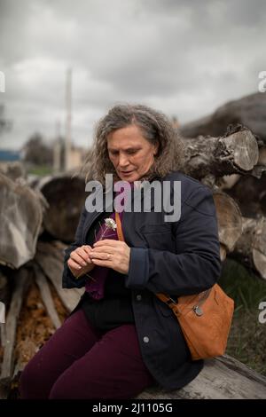 Une femme de 60 ans, aux cheveux gris, assise, regardant attentivement une petite fleur, au printemps, dans une zone rurale de la région de Campo de Borja, Zarag Banque D'Images