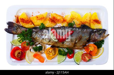Photo de truite entière savoureuse cuite avec pommes de terre, légumes verts et tomates Banque D'Images