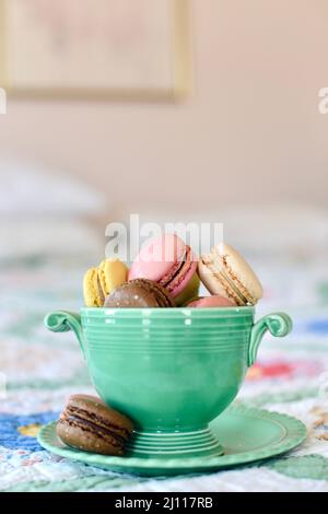 Gros plan des biscuits au macaron français dans un bol vert vintage sur un lit. Banque D'Images