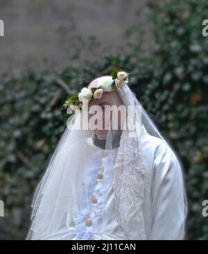 Enciso, Espagne – 5 mars 2022 : homme timide vêtu d'une robe de mariage blanche et d'une couronne de fleur sur sa tête, en regardant loin. Carnaval traditionnel d'Enciso. Banque D'Images