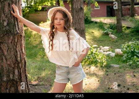 Préadolescence penchée fille de grand tronc d'arbre dans cour verte de la maison de campagne Banque D'Images