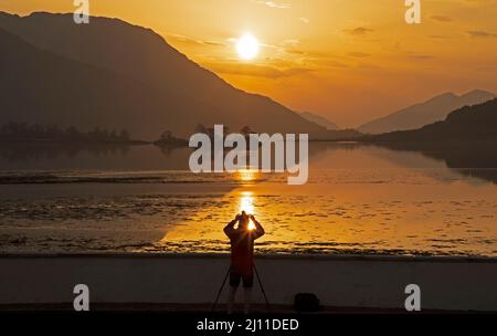 Loch Leven, Ballachulish, Écosse, Royaume-Uni. 21st mars 2022. Coucher de soleil sur le Loch Leven en regardant vers le pont de Ballachulish. Photo : le photographe ajuste les paramètres de son appareil photo pour le soleil couchant, après un après-midi de brume. Crédit : Arch White/Alamy Live News Banque D'Images