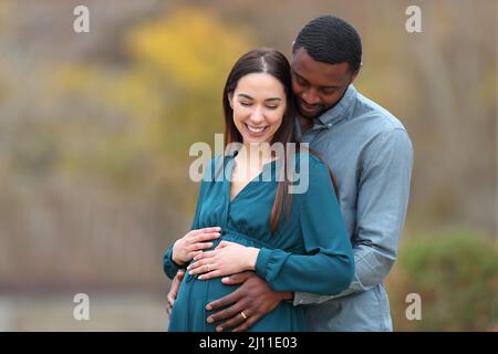 Heureux couple interracial regardant le ventre enceinte dans un parc Banque D'Images