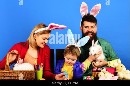 Bonne famille célébrant le jour de Pâques. Mère, père et fils aux oreilles de lapin assis à une table en bois. Banque D'Images