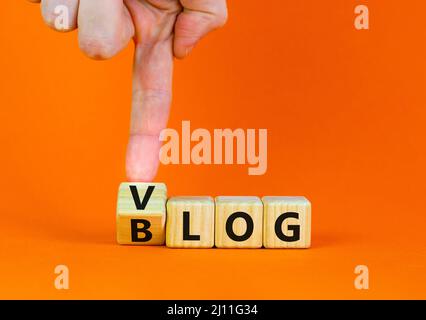 Blog ou symbole Vlog. Homme d'affaires tourne des cubes en bois et change le mot Blog à Vlog. Belle table orange fond orange. Business et informat Banque D'Images