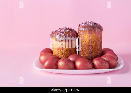 Deux gâteaux de Pâques et œufs colorés sur plaque blanche sur fond rose Banque D'Images