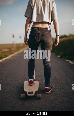 belle fille se tient sur un long-board une jambe.affiche, bannière verticale, photographie anonyme. sans visage . Jour ensoleillé . Banque D'Images