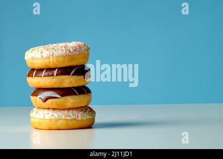 Quatre délicieux beignets frais avec des saupoudres de couleurs différentes et avec du chocolat se trouvent à côté l'un de l'autre, l'un sur l'autre Banque D'Images