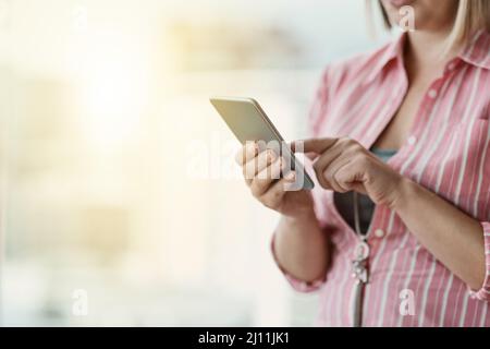 Rester connecté et en boucle. Photo rognée d'une femme d'affaires non identifiable utilisant un téléphone portable dans un bureau. Banque D'Images