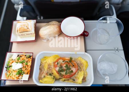 Menu avion sur plateau repas végétarien avec pâtes, salade, gâteau, pain et verres en plastique vides dans l'avion Banque D'Images