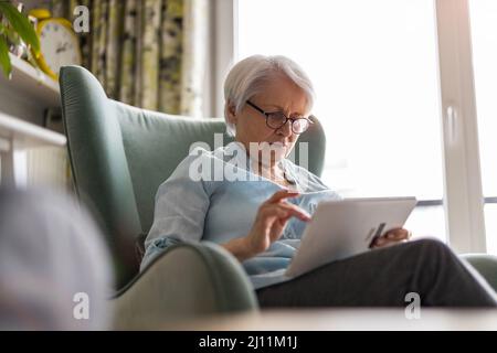 Femme âgée utilisant une tablette numérique à la maison Banque D'Images