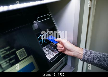 Gros plan sur la main d'un homme qui présente une carte de crédit bleue à un distributeur automatique de billets Banque D'Images