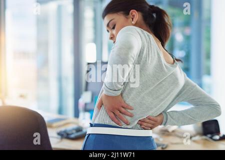 Quelle est cette forte piqûre dans mon dos. Photo d'une jeune femme d'affaires souffrant de douleurs dorsales pendant qu'elle travaille dans un bureau. Banque D'Images