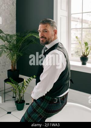 beau mûr courageux et élégant homme d'affaires écossais dans le kilt et le costume dans la salle de bains. Style, travail à la maison, mode, style de vie, culture, ethnique Banque D'Images