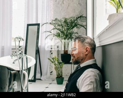 beau mûr courageux et élégant homme d'affaires écossais dans le kilt et le costume dans la salle de bains. Style, travail à la maison, mode, style de vie, culture, ethnique Banque D'Images