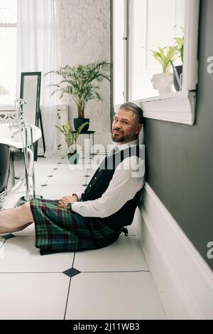 beau mûr courageux et élégant homme d'affaires écossais dans le kilt et le costume dans la salle de bains. Style, travail à la maison, mode, style de vie, culture, ethnique Banque D'Images