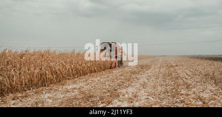 Récolte de maïs dans un champ par une récolteuse rouge, un jour d'automne nuageux Banque D'Images