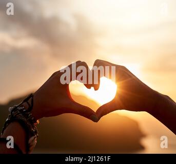 J'adore ce sentiment de vacances. Prise de vue rognée d'une personne non identifiable faisant une forme de coeur avec ses mains au coucher du soleil. Banque D'Images