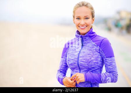 Se mettre en forme et l'aimer. Portrait d'une jeune femme en vêtements de sport debout à la plage. Banque D'Images