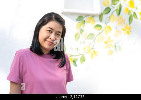 Portrait d'une femme asiatique d'âge moyen avec mur blanc d'une maison de villégiature et style vintage peint pour la décoration, visage souriant, cheveux courts noirs, Banque D'Images