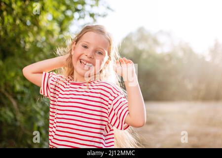 Portrait d'une petite fille aux cheveux blonds ondulés profitant du soleil couchant Banque D'Images