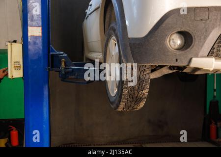 voiture argentée soulevée par ascenseur à l'atelier de réparation automobile Banque D'Images