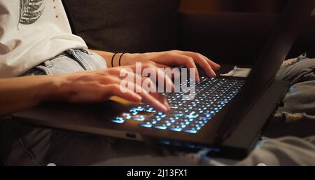 Gros plan femme mains travaillant dactylographiant sur clavier ordinateur portable dans la pièce sombre assis sur le canapé. Travailleur indépendant utilisant un ordinateur portable travaillant à domicile Banque D'Images