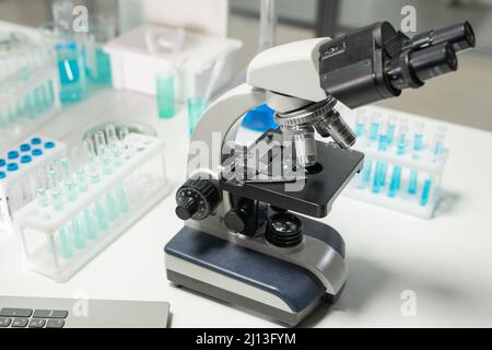 Microscope entouré de groupes de flacons contenant de la substance chimique liquide bleue et se tenant sur un bureau en laboratoire Banque D'Images