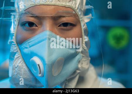 Femme asiatique chimiste ou professionnel de la santé en costume blanc à risque biologique, respirateur et écran facial de protection regardant la caméra Banque D'Images