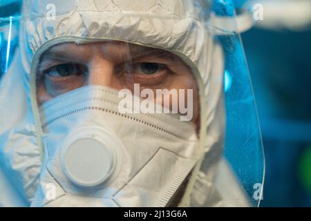 Virologiste ou chercheur mâle mature en costume blanc à risque biologique, respirateur et écran facial de protection regardant la caméra Banque D'Images