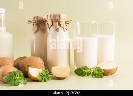 deux tasses et plusieurs bouteilles remplies de lait de pomme de terre végétale sur fond pastel avec des tubercules et des tranches de pommes de terre fraîches Banque D'Images