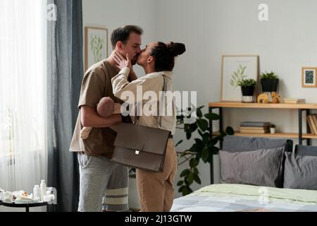 Un jeune couple affectueux partage son baiser le matin tandis qu'une femme va partir avec bébé et son mari qui reste à la maison Banque D'Images